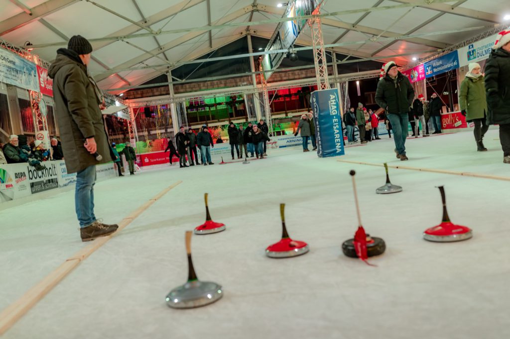 Mehrere Personen beim Eisstockschießen stehen auf der Eisfläche; Eisstöcke im Vordergrund